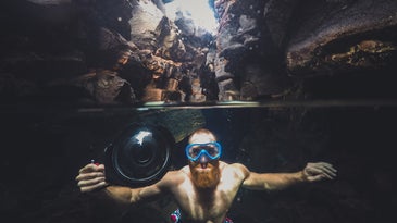 man with a beard underwater holding a camera with an underwater camera case
