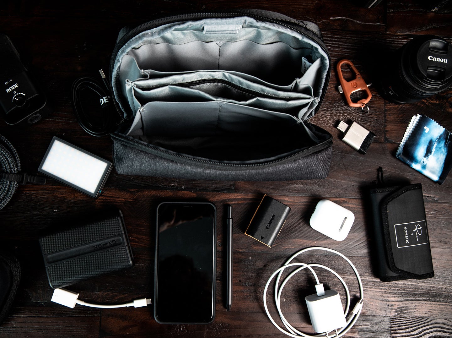 camera, phone, charger, flash drive, and camera bag on a wooden table