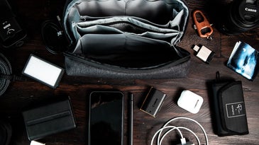 camera, phone, charger, flash drive, and camera bag on a wooden table