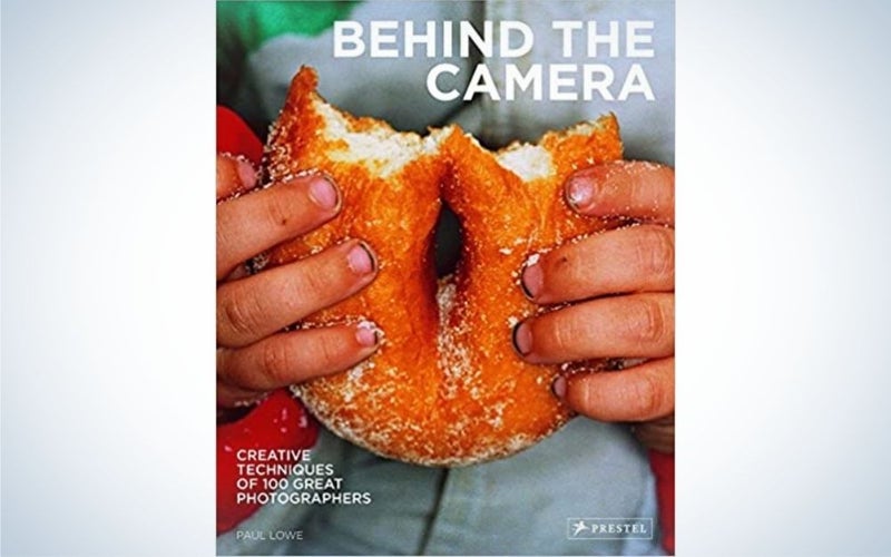 The hands of a child holding a bitten donut and an inscription that says "Behind the camera".