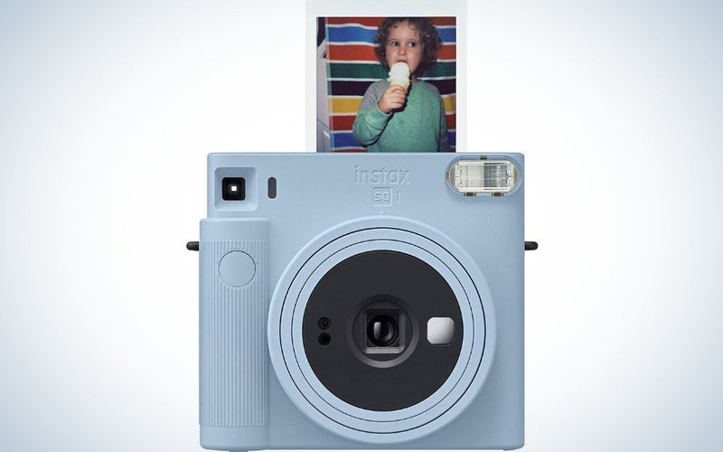 A glacier blue Fujifilm Instax Square SQ1 instant camera in square form from the front with a picture of a toddler eating ice cream on top of it.