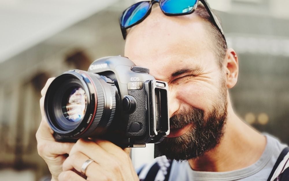 A man with blue sunglasses over his head taking a picture with a professional camera on his hands.