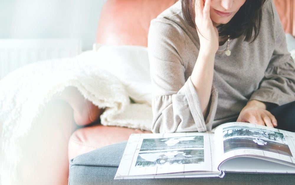 Woman with grey shirt sitting on a pink sofa and staring a photo album.