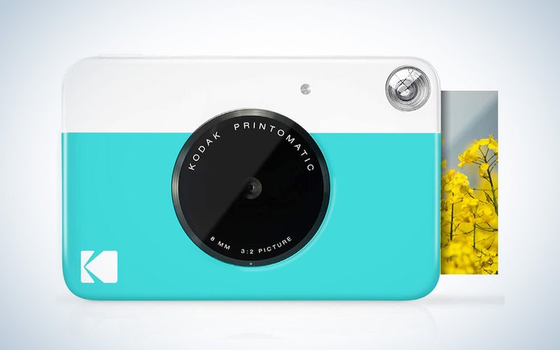 One of the best Kodak instant camera models, a white and teal model, printing a photo out of its side.