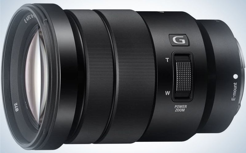 An all-black lens of a professional camera which looks sideways and with a light-colored glass front lens.
