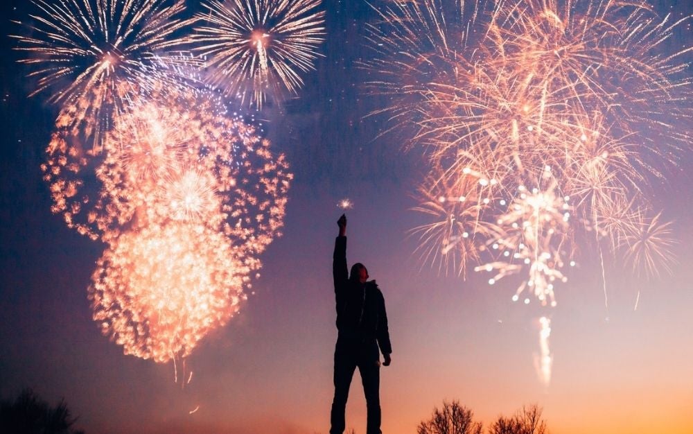 A man raising his hand and watching the fireworks shining in the sky.