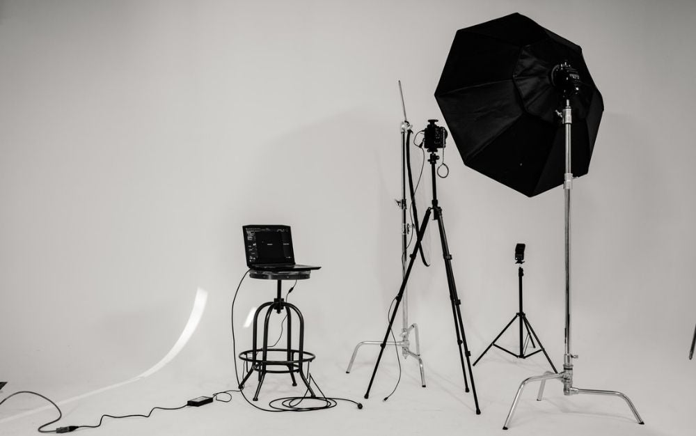 A photo studio which has some light black and white umbrellas as well as some bags and sets that help in the photography process.