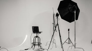 A photo studio which has some light black and white umbrellas as well as some bags and sets that help in the photography process.