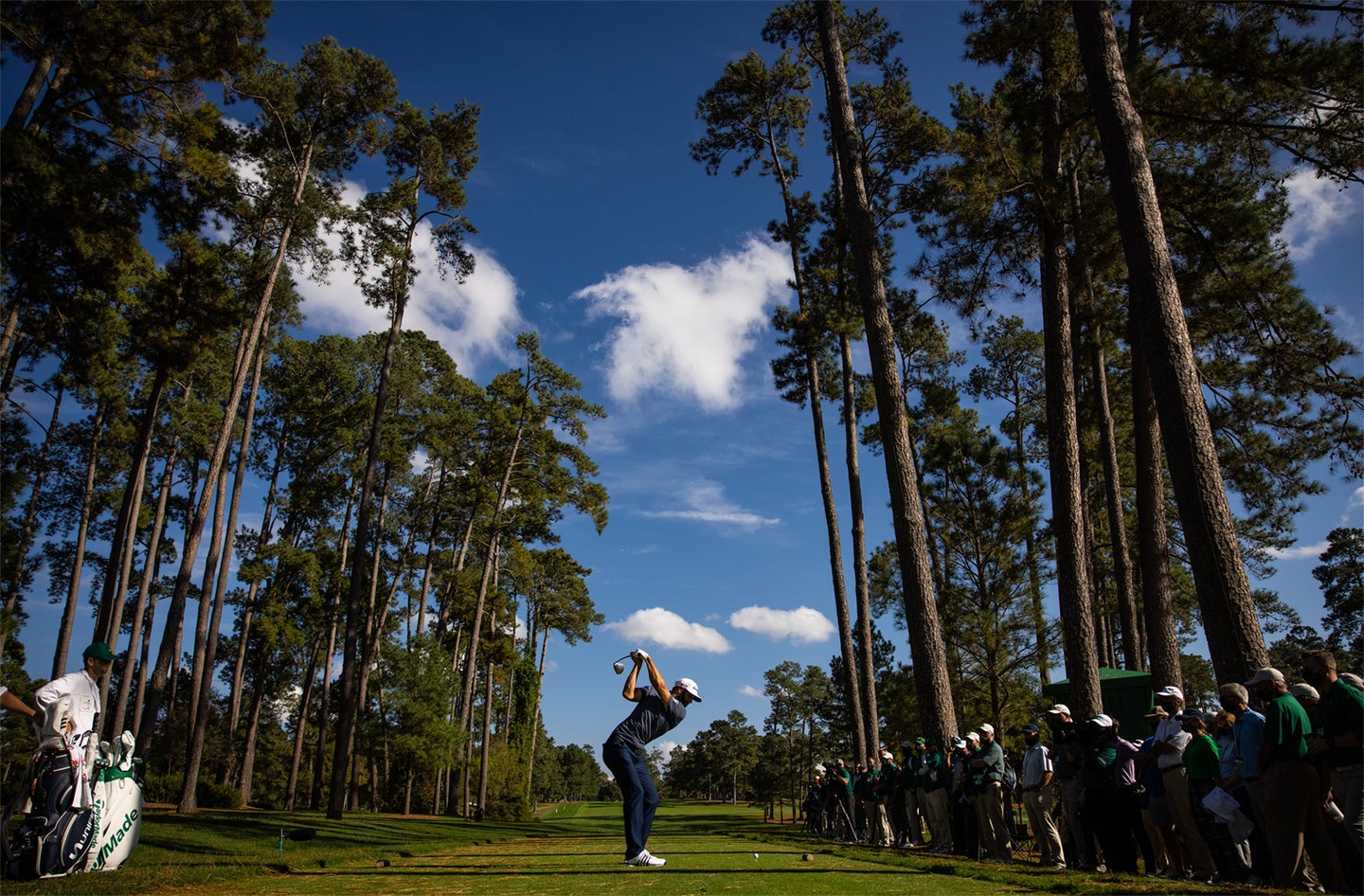 A golfer teeing off between tall trees.