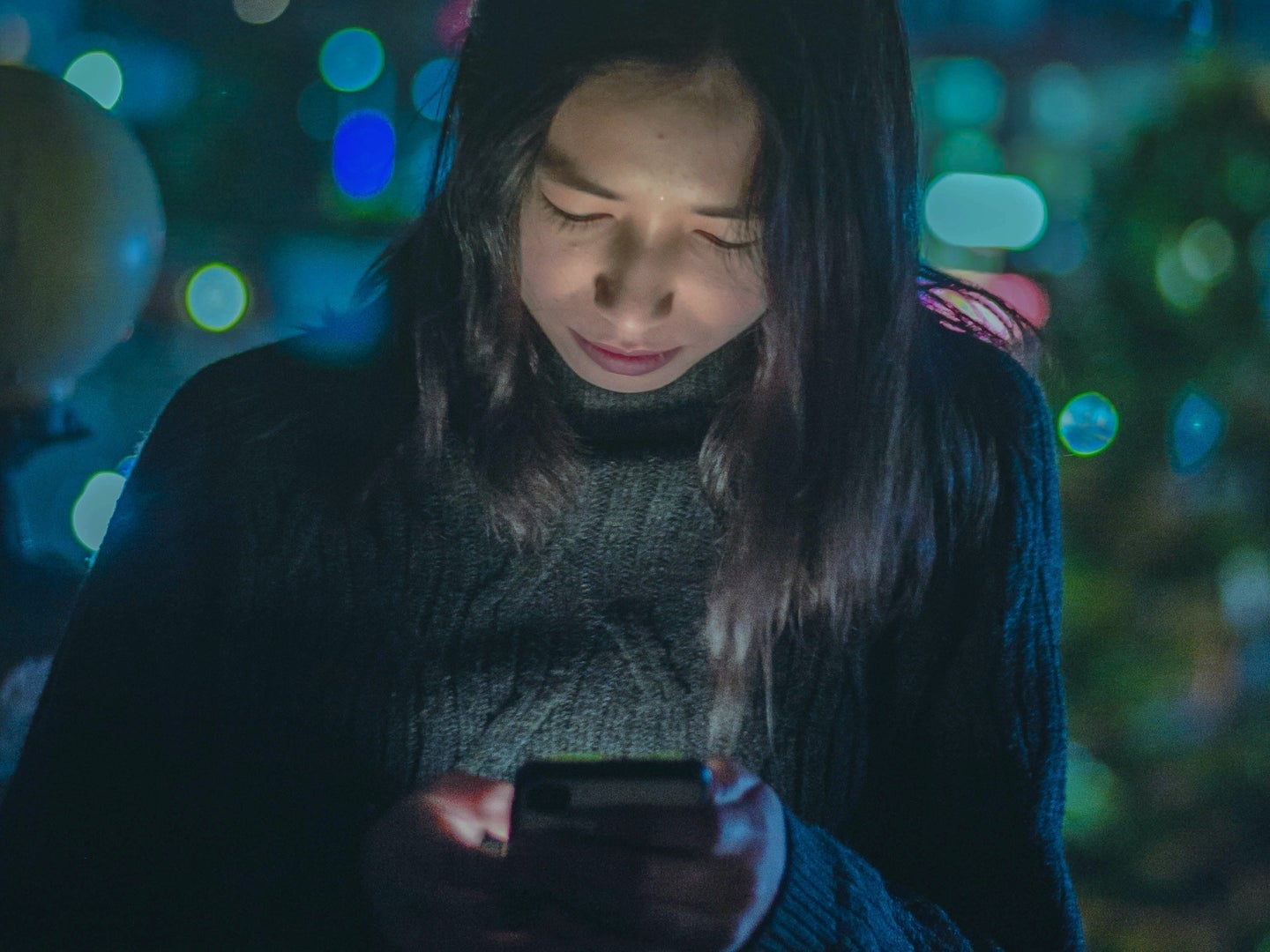 A woman looking at her phone screen at night while the screen illuminates her face