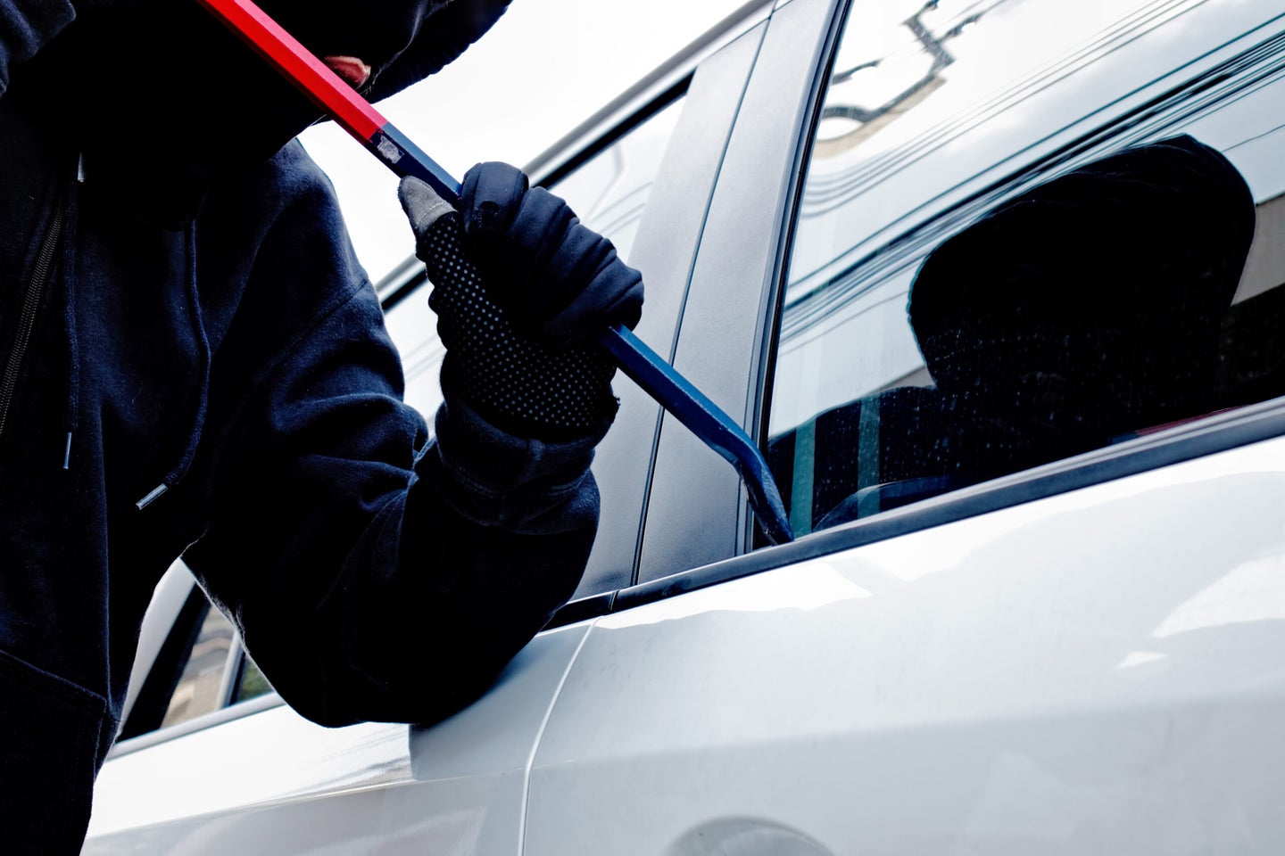 A masked person trying to break into a car.