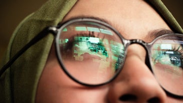 A women with glasses and the reflection of a computer screen in her lenses.