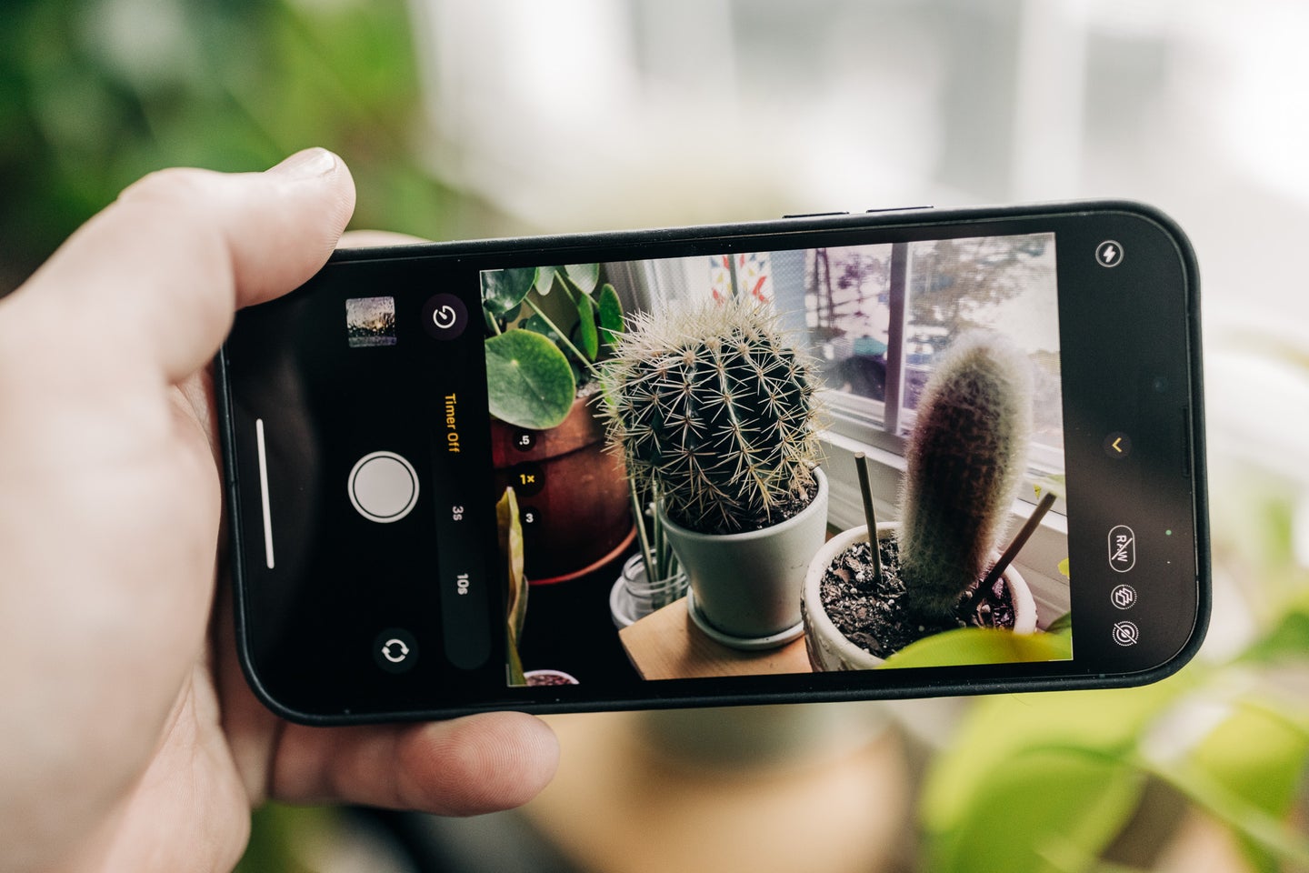 A hand holding an iphone with the camera app on screen and the self-timer enabled