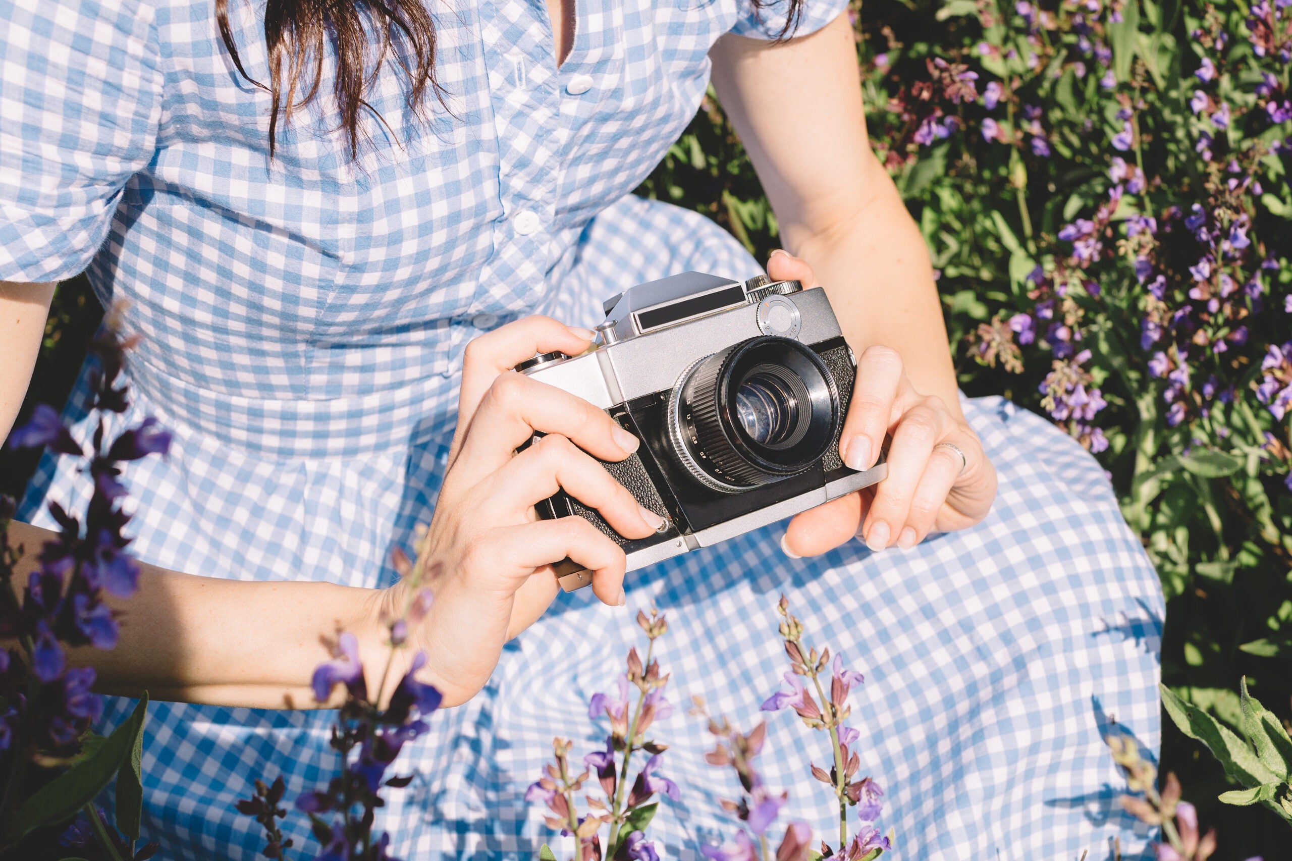 Câmera nas mãos de uma mulher branca em um vestido azul em um fundo de flores de lavanda ao ar livre