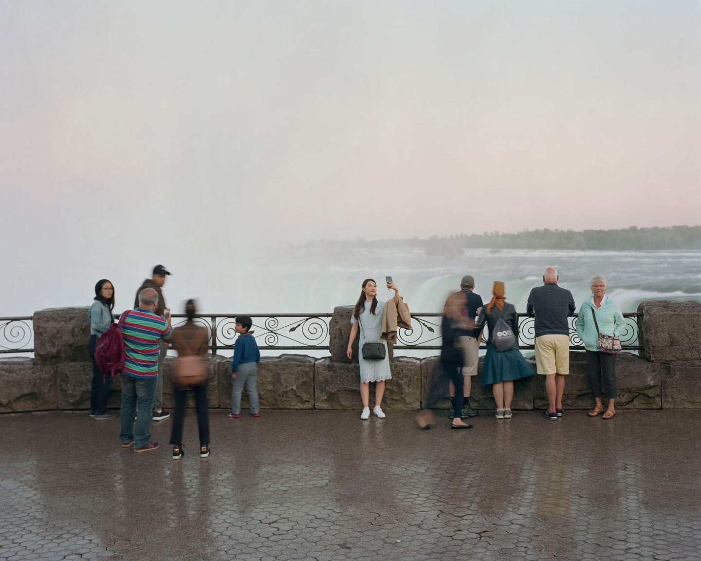 A film photo showing a small crowd gathered with a waterfall in the background. Many are taking selfies.