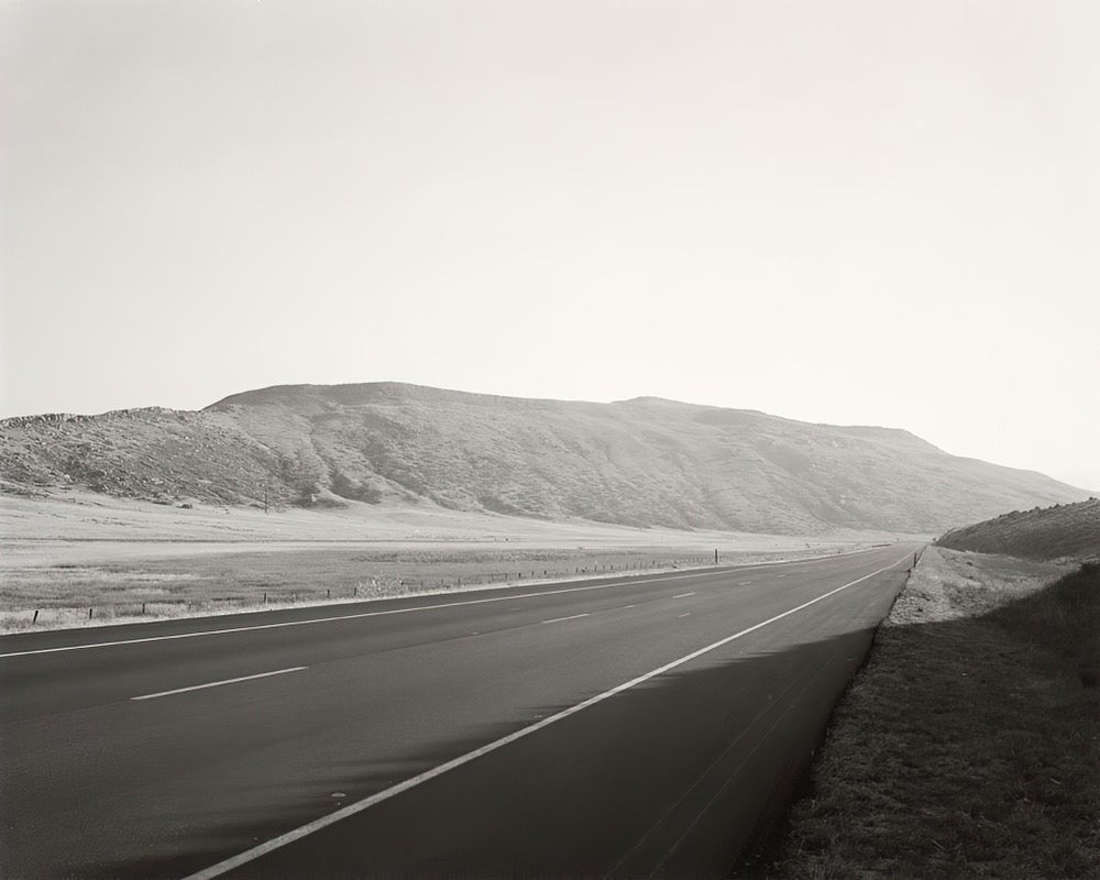 A B&W film photo of a an empty roadway surrounded by hills.