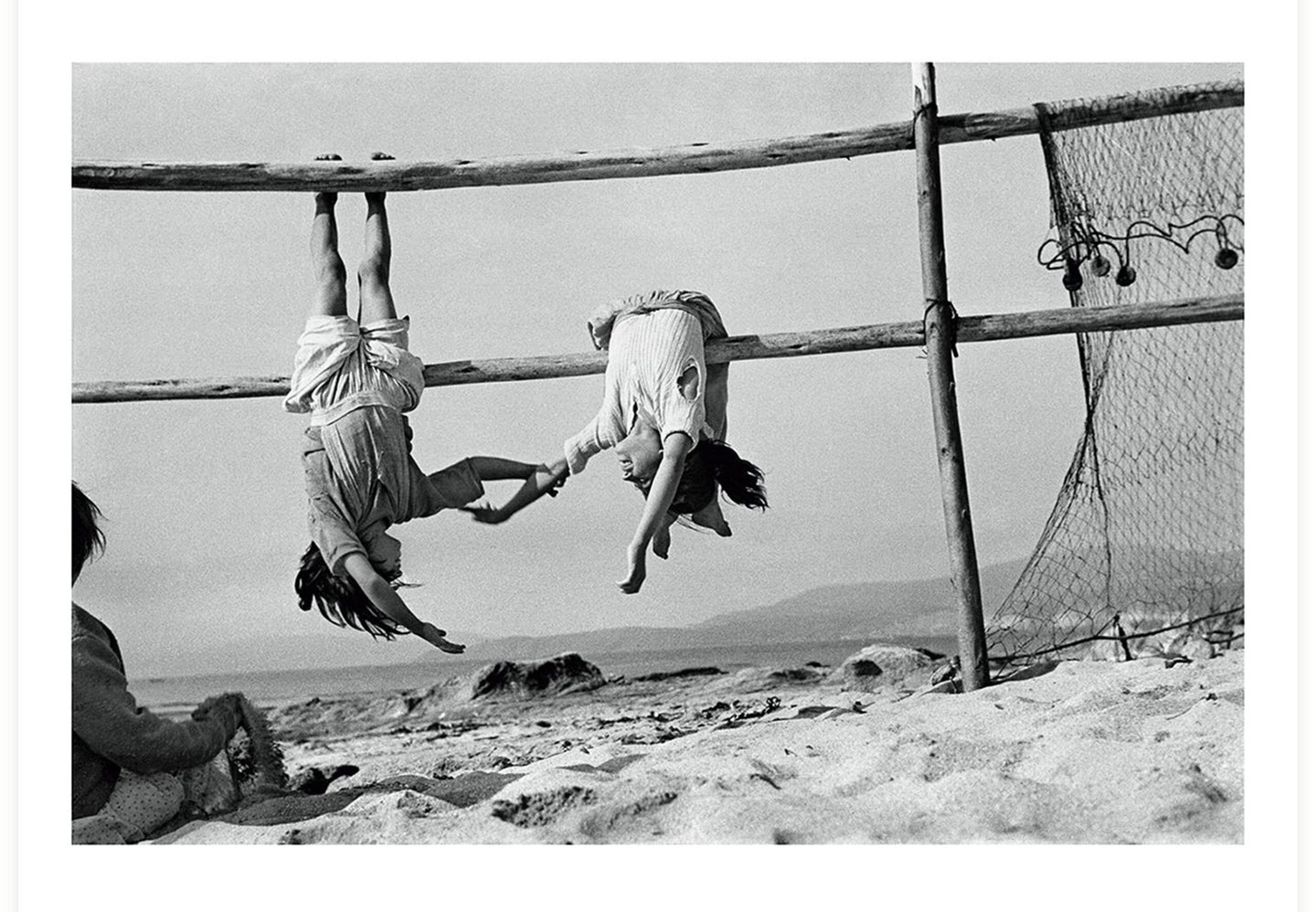 Two young women play on a fence on the beach.