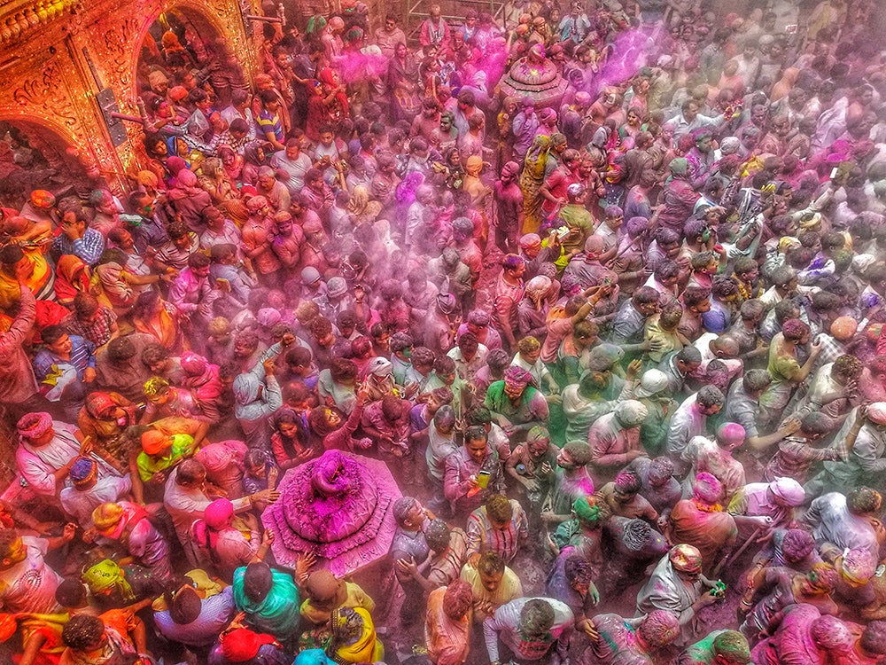 The Holi celebration, this image shows a crowd of people in coated in pink, purple and yellow dyes.