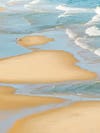 A beach scene from above with just one person playing in the water and sand.