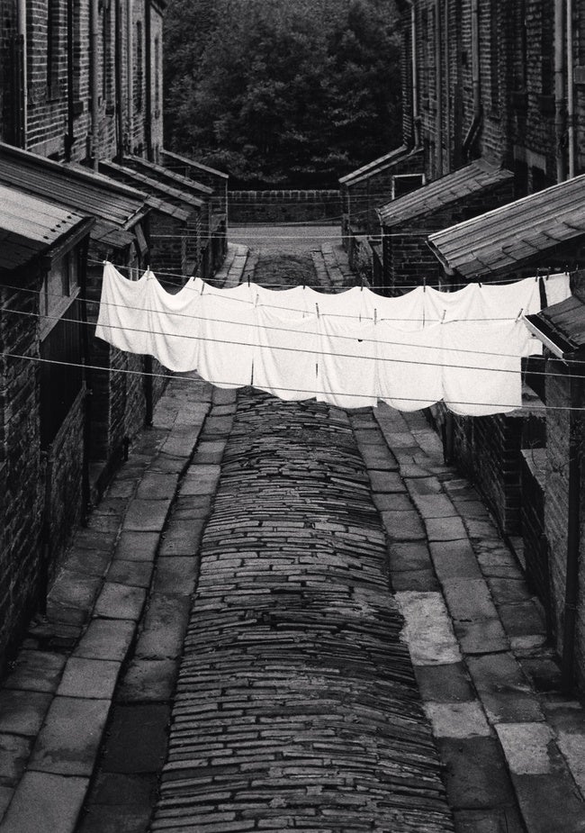 A black and white photo of laundry hanging on a line in a deserted street.