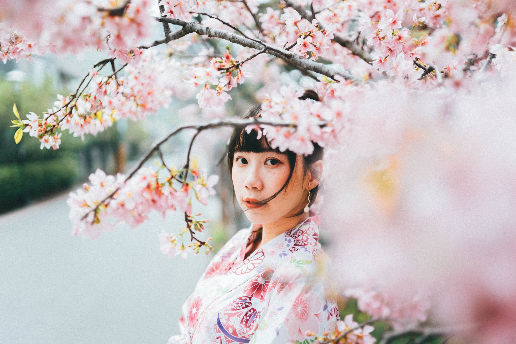 A women dressed in pink poses for a photo in front of a cherry blossoms 