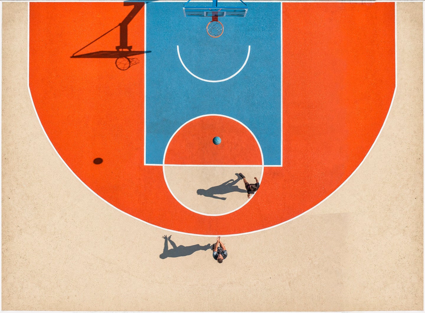 Two people on an orange, blue, and tan basketball court, from above.