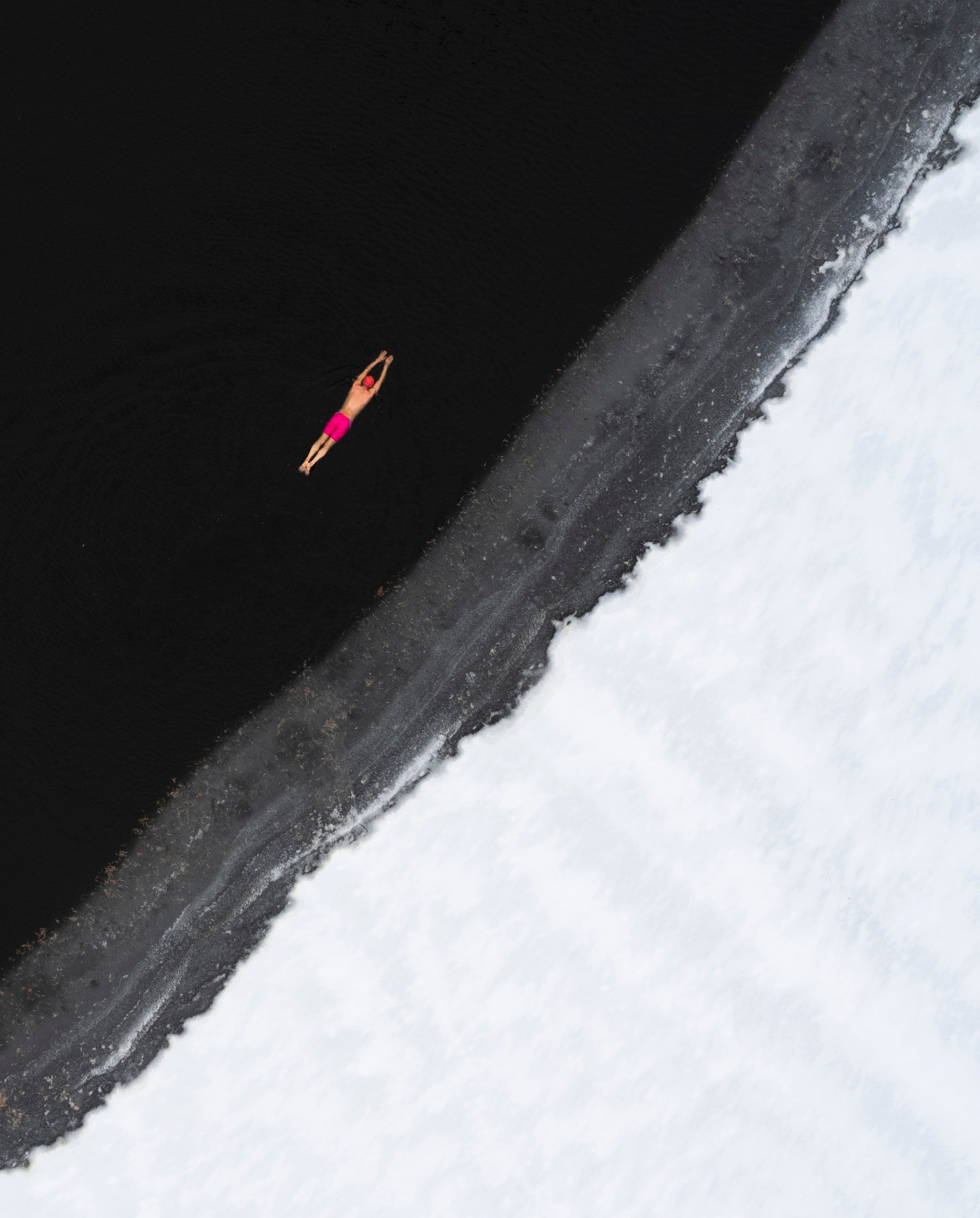 A man in a pink bathing suit swims in a nearly frozen body of water.