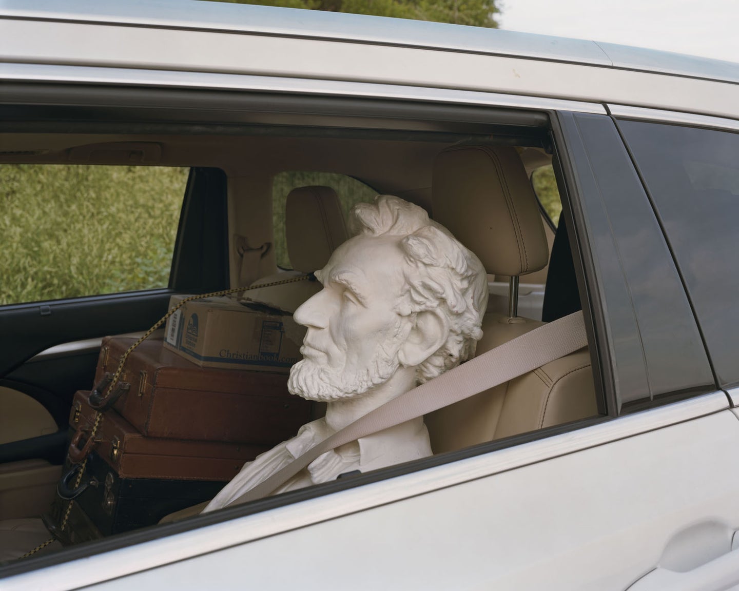 A bust of Abe Lincoln's head in the backseat of a car, window open.