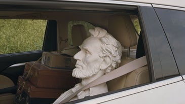 A bust of Abe Lincoln's head in the backseat of a car, window open.