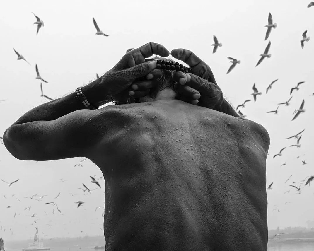 A man puts prayer beads around his neck as seagulls fly through the sky above