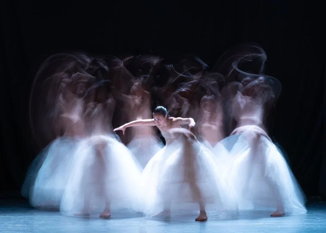 A long exposure captures the blurred movement of a dance troop wearing white tulle skirts