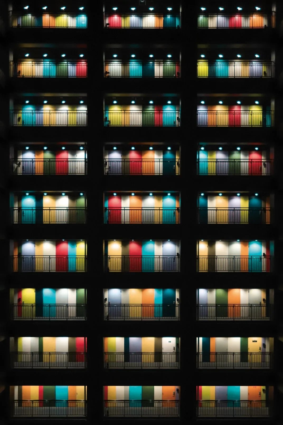 Colorful office doors are illuminated by harsh white lights in the pitch black of night