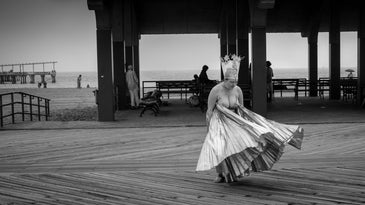 black and white photo of a woman's skirt flutters in the wind as she stands on a pier