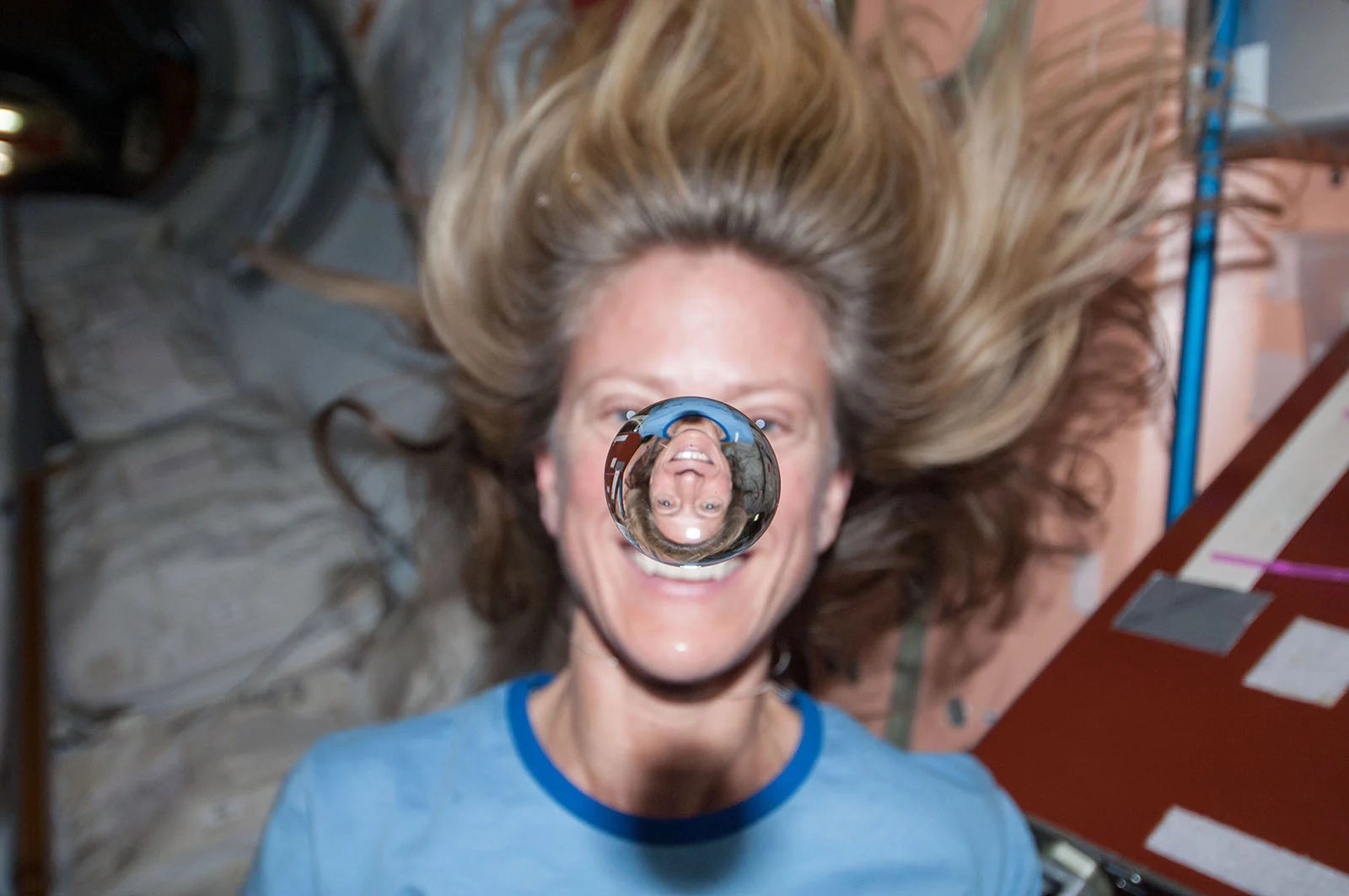 NASA astronaut Karen Nyberg watches a water bubble float freely between her and the camera, showing her image refracted in the droplet.