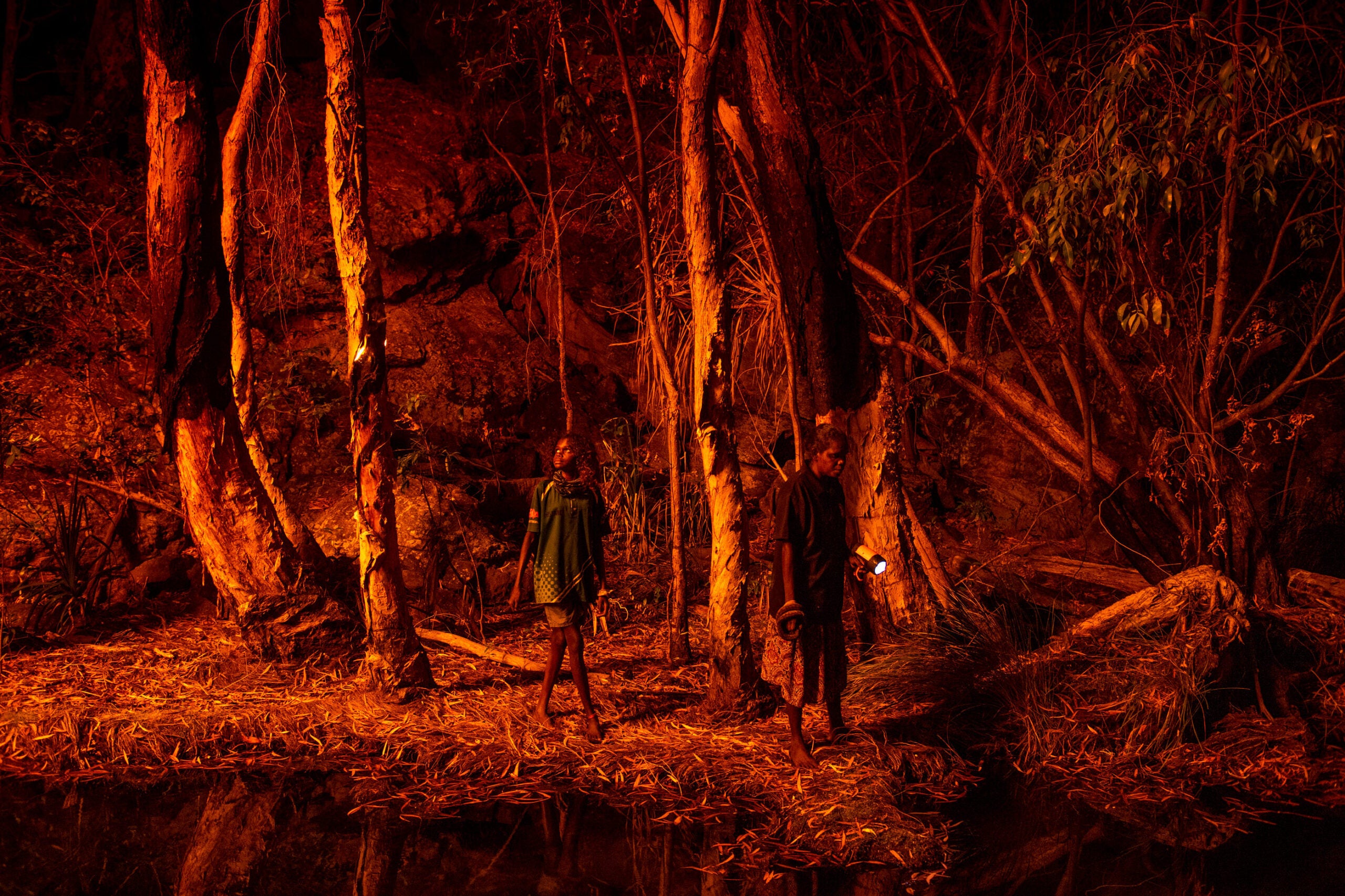 Stacey Lee (11, left) sets the bark of trees alight to produce a natural light source to help hunt for file snakes (Acrochordus arafurae), in Djulkar, Arnhem Land, Australia, on 22 July 2021.