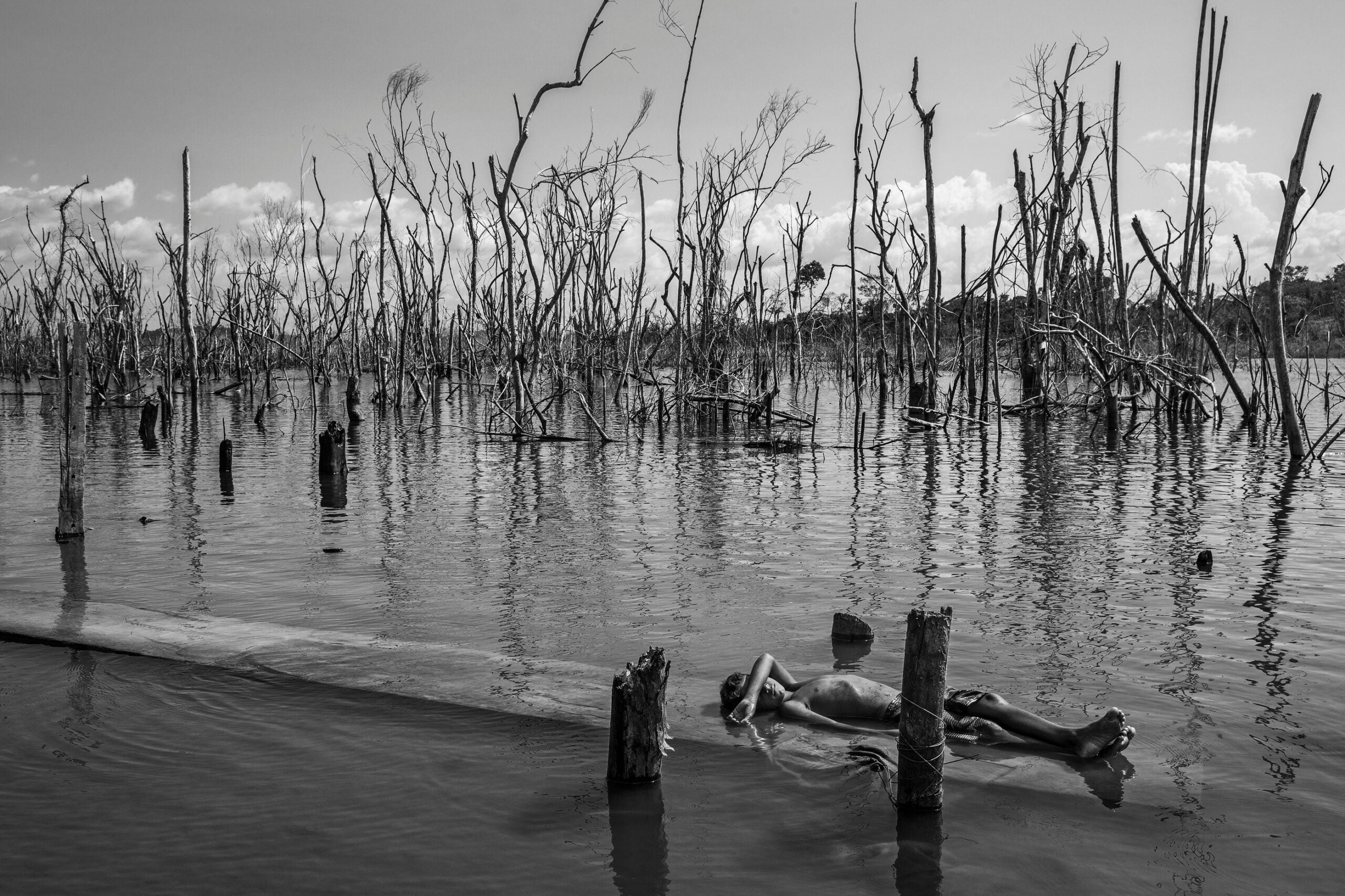 A boy rests on a dead tree trunk in the Xingu River in Paratizão, a community located near the Belo Monte hydroelectric dam, Pará, Brazil, on 28 August 2018. He is surrounded by patches of dead trees, formed after the flooding of the reservoir.