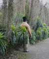 a man in a top hat stands between short palm trees 