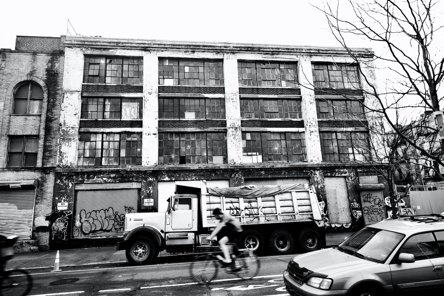 black and white photo on a busy city street. a biker whizzes by among trucks and cars