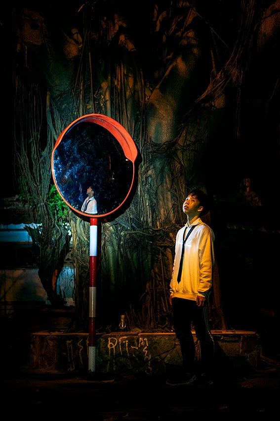 boy stands facing an orange glow, a mirror reflects him in the background