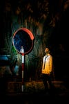 boy stands facing an orange glow, a mirror reflects him in the background