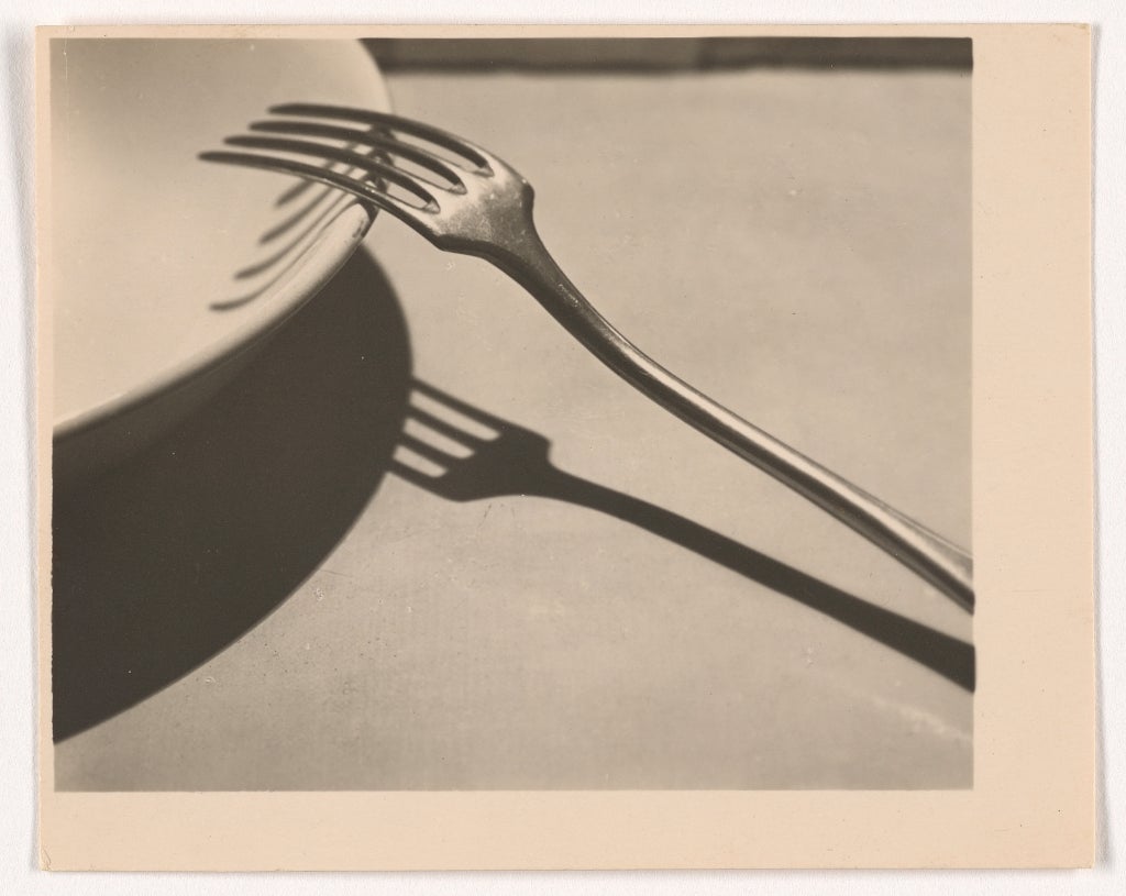 A B&W photo of a fork on a plate with a heavy shadow.
