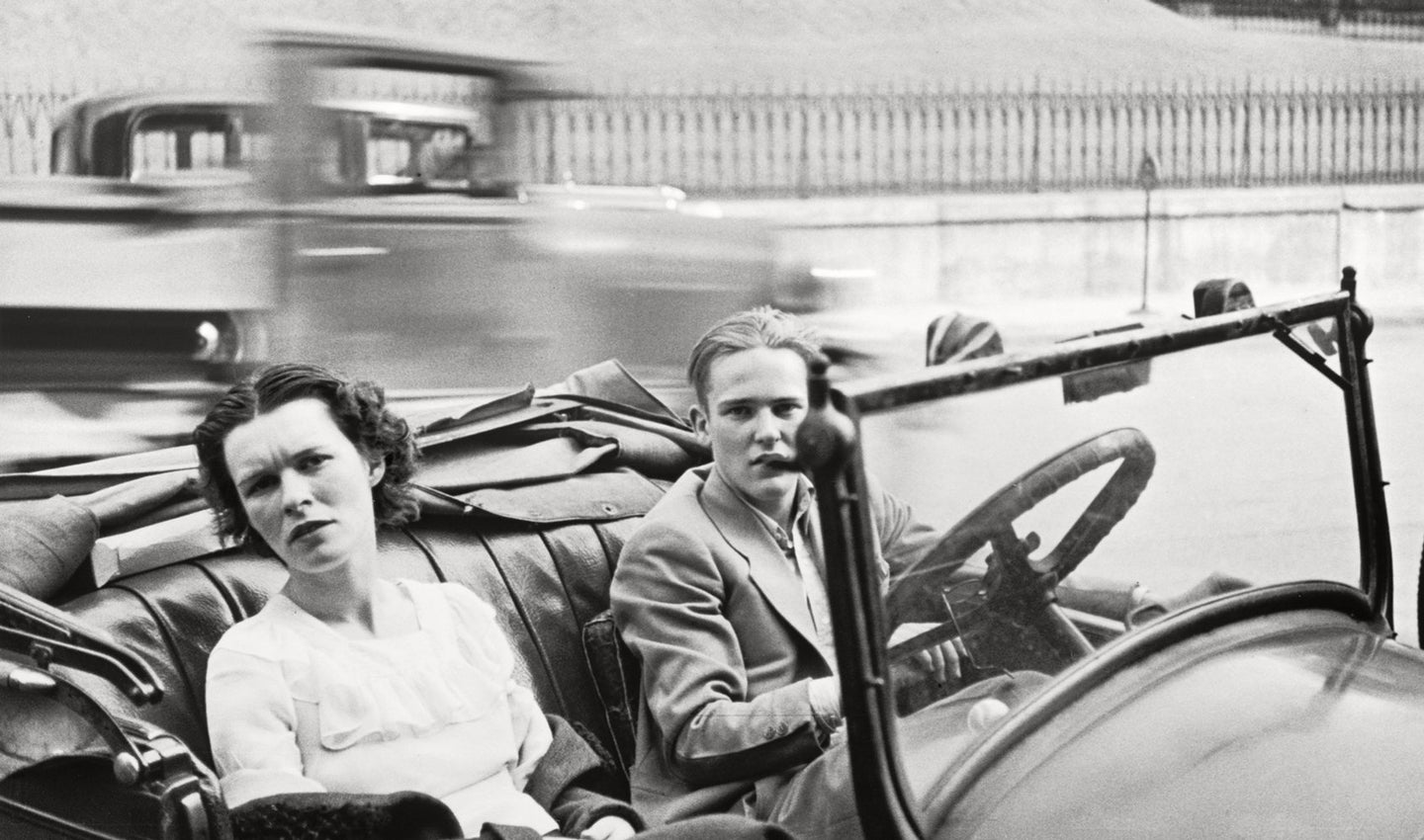 B&W photo of two women in a parked convertible.