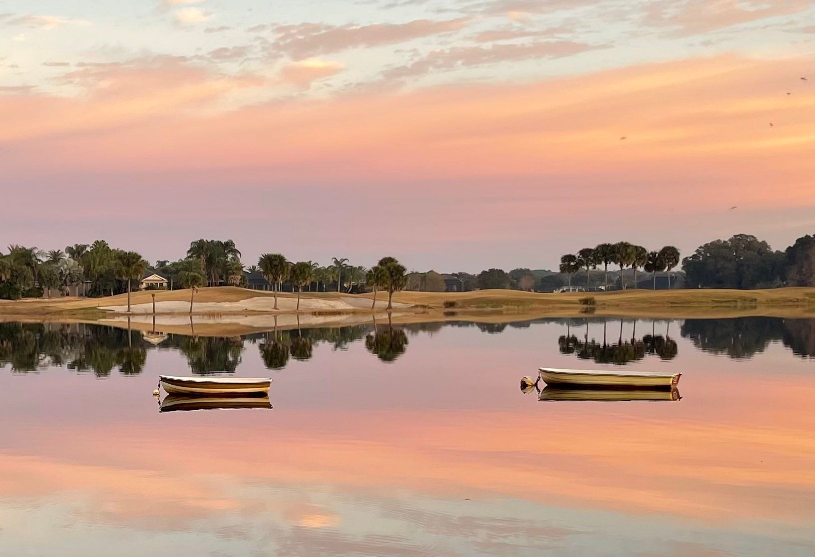 orange, purple, and pink sunrise on a lake with two boats on the water in florida