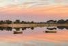 orange, purple, and pink sunrise on a lake with two boats on the water in florida