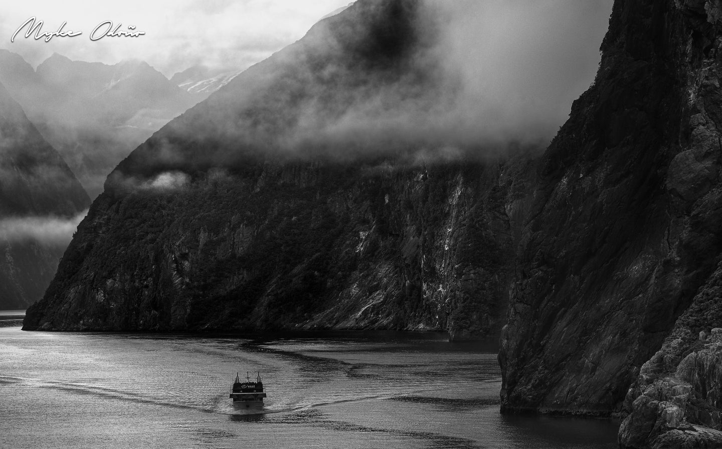 black and white photo of the Fiordlands National Park, New Zealand, with a boat being dwarfed by the cliffsides