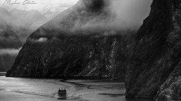 black and white photo of the Fiordlands National Park, New Zealand, with a boat being dwarfed by the cliffsides