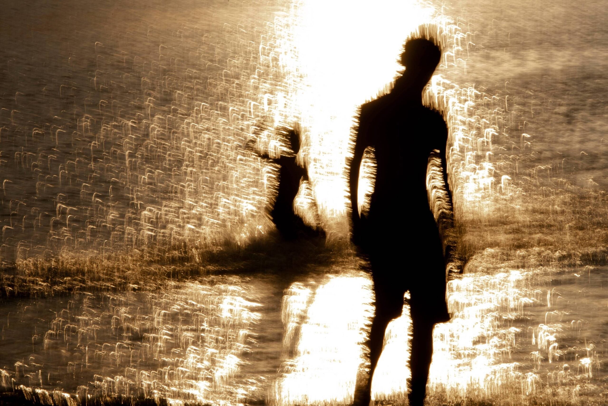 silhouette of two people on the beach at sunset. the water is glistening from the puddle of sunlight