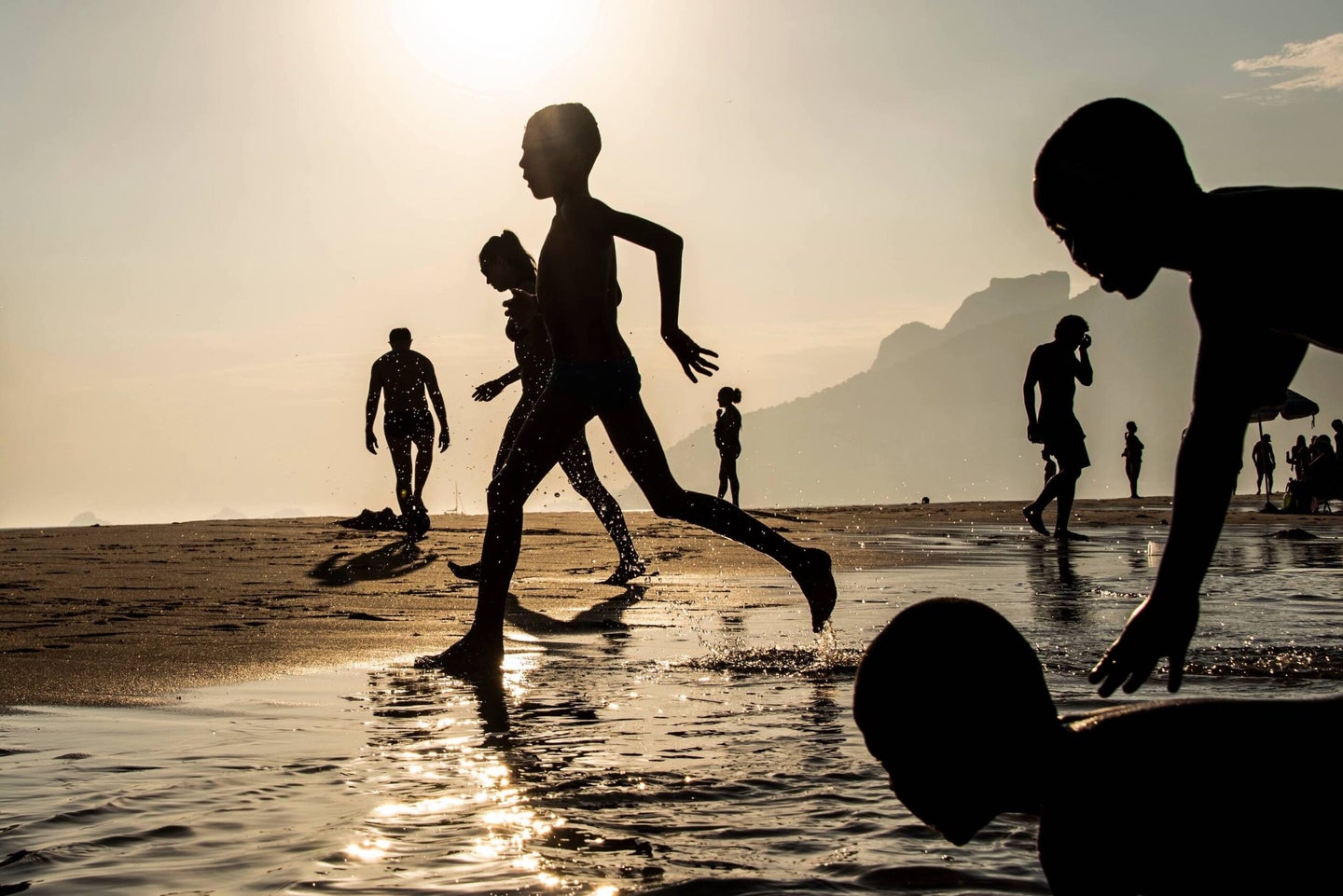 silhouette of children running towards the water on the beach