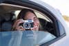 Woman sitting in car, taking pictures with a camera