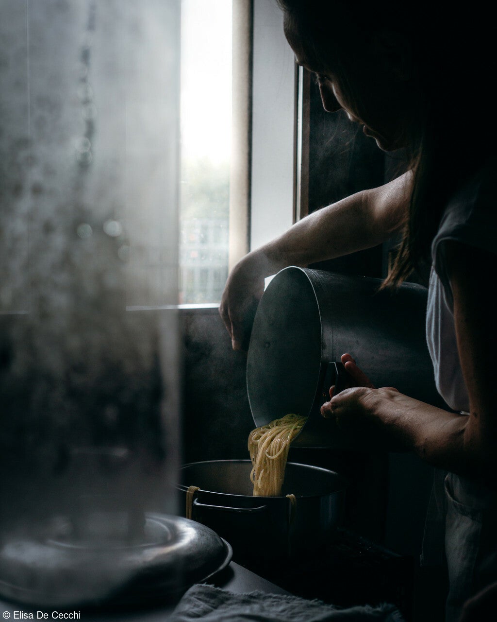 uma pessoa drena macarrão pela janela da cozinha em um dia sombrio e nublado